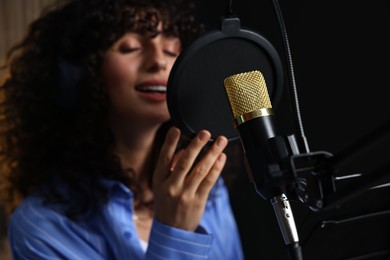 Photo of Vocalist singing into microphone in professional record studio, selective focus