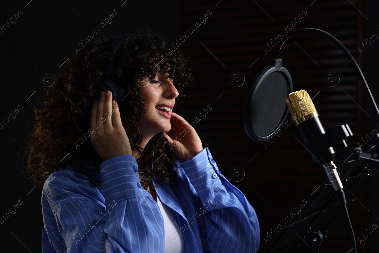 Photo of Vocalist with headphones singing into microphone in professional record studio