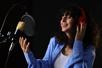 Photo of Vocalist with headphones singing into microphone in professional record studio