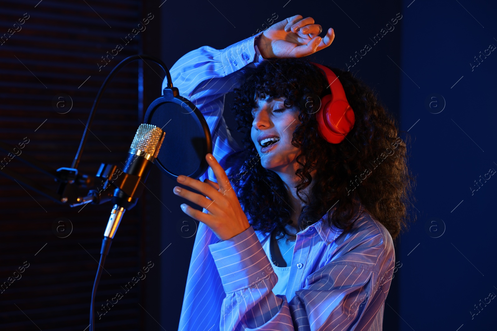 Photo of Vocalist singing into microphone in professional record studio with color lights