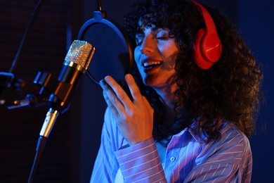 Photo of Vocalist singing into microphone in professional record studio with color lights