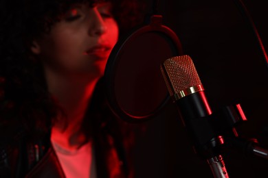 Photo of Woman singing into microphone in professional record studio with red light, selective focus