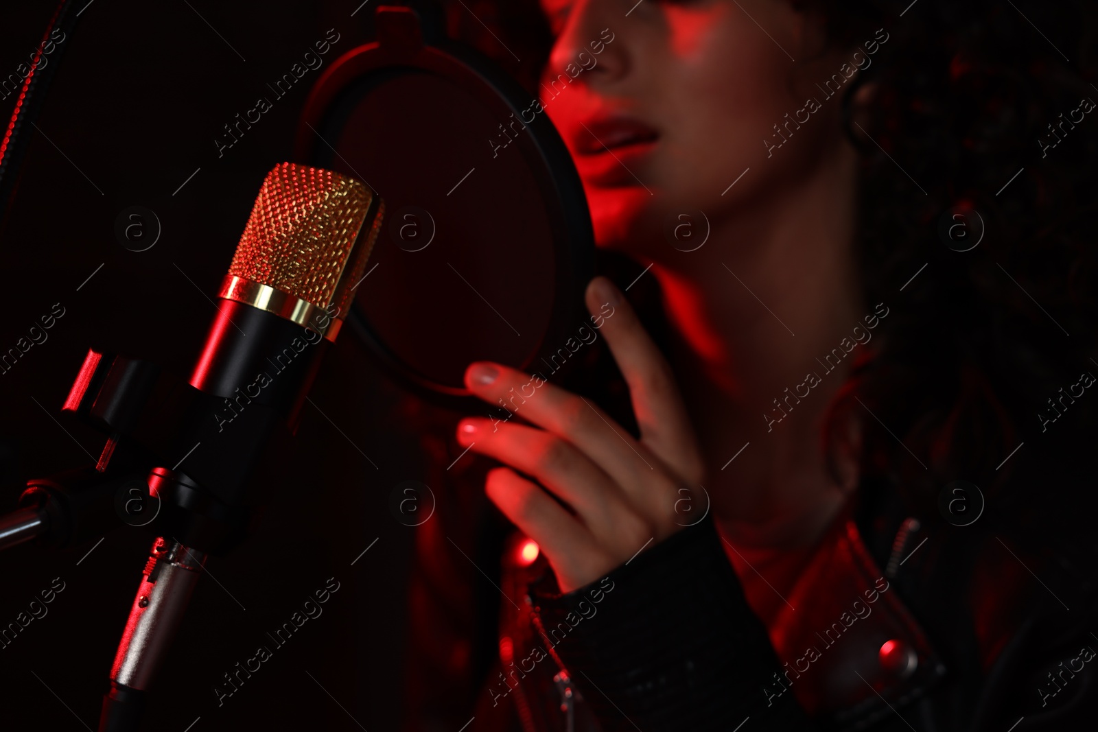 Photo of Woman singing into microphone in professional record studio with red light, closeup