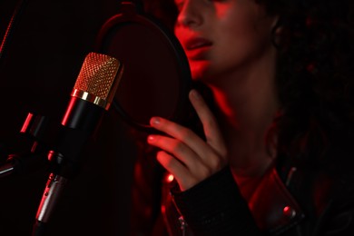 Photo of Woman singing into microphone in professional record studio with red light, closeup