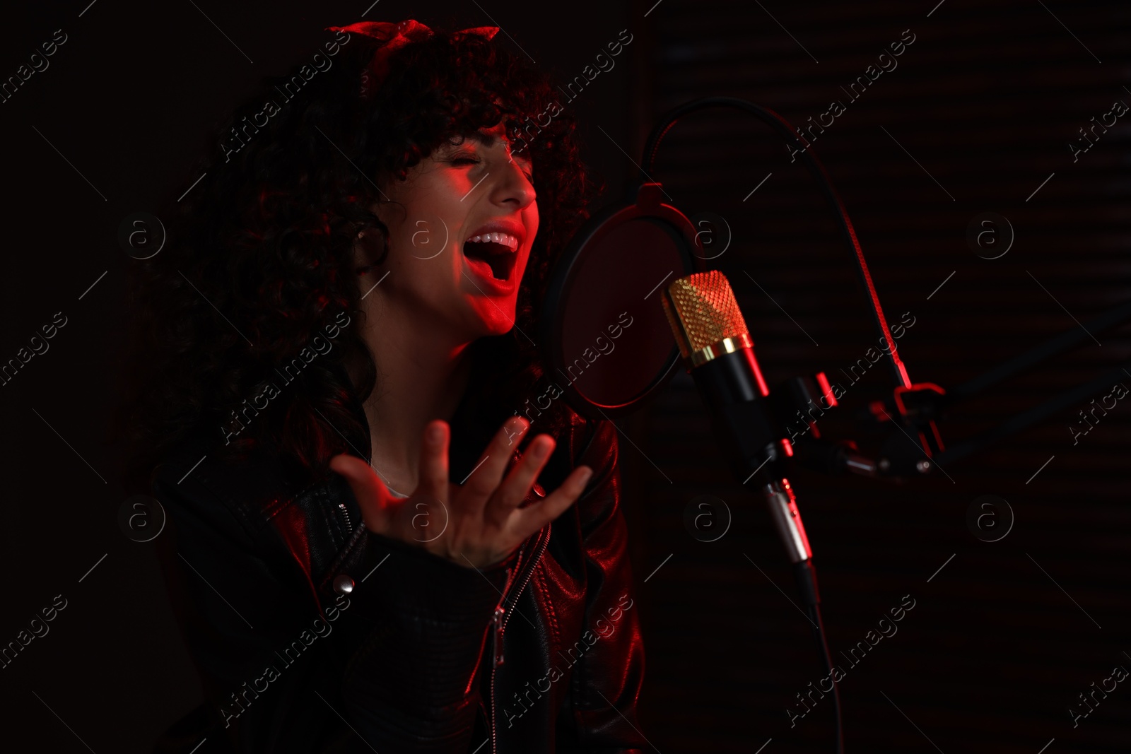 Photo of Vocalist singing into microphone in professional record studio with red light