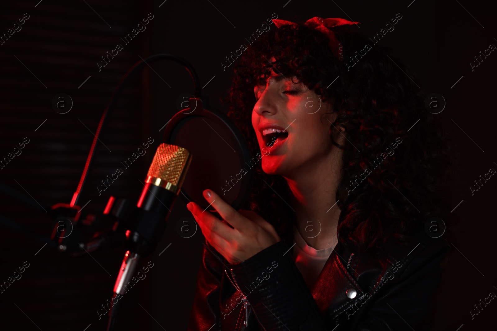 Photo of Vocalist singing into microphone in professional record studio with red light