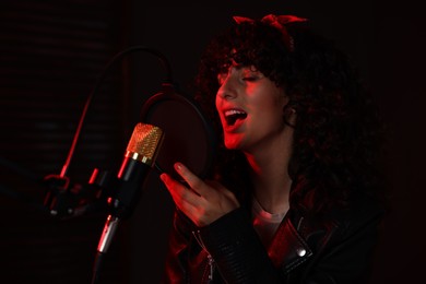 Photo of Vocalist singing into microphone in professional record studio with red light