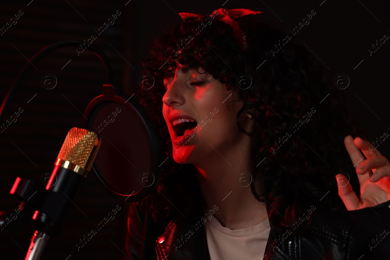 Photo of Vocalist singing into microphone in professional record studio with red light