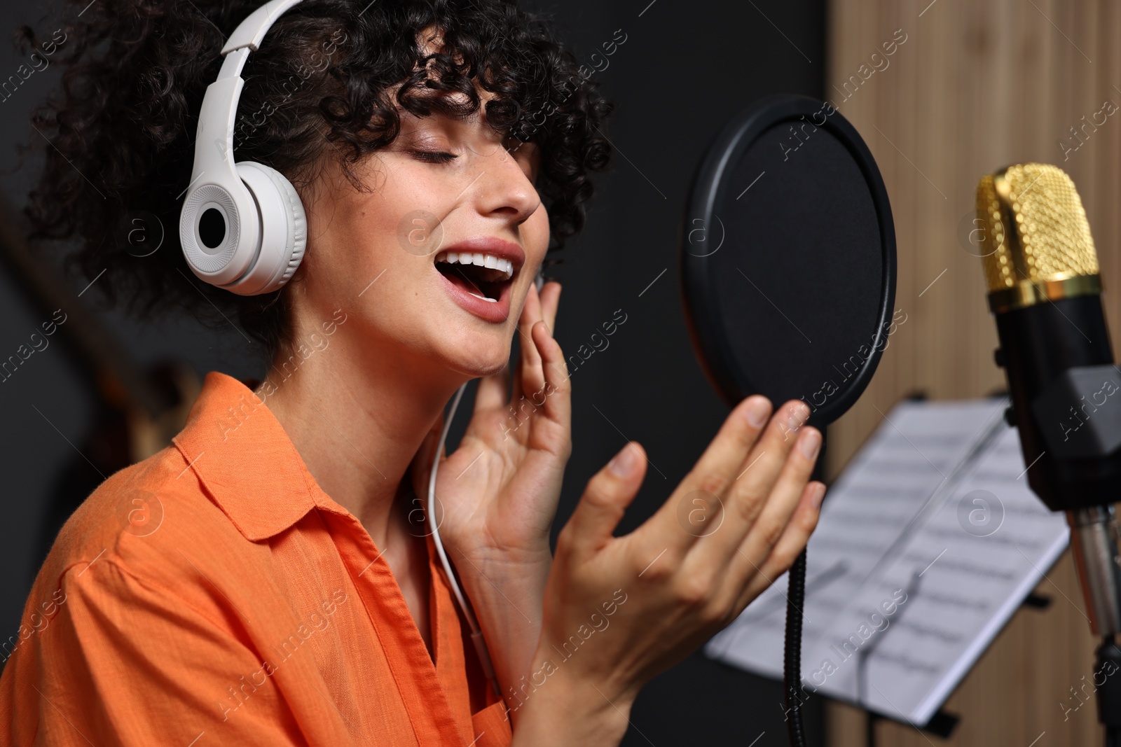 Photo of Vocalist with headphones singing into microphone in professional record studio