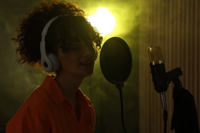 Photo of Vocalist wearing headphones singing into microphone in professional record studio with smoke and lights
