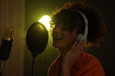 Photo of Vocalist wearing headphones singing into microphone in professional record studio with smoke and lights