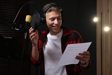 Photo of Singer with sheet recording song in professional studio