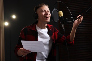 Photo of Singer with sheet recording song in professional studio