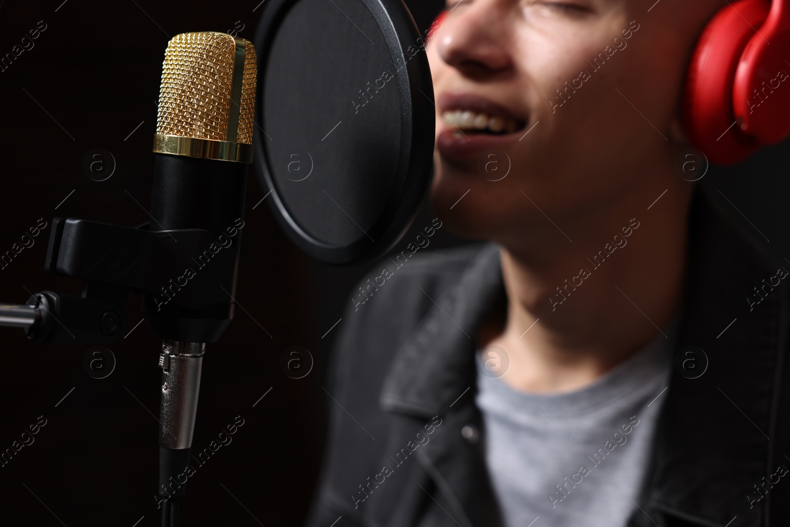 Photo of Vocalist singing into microphone in professional record studio, closeup