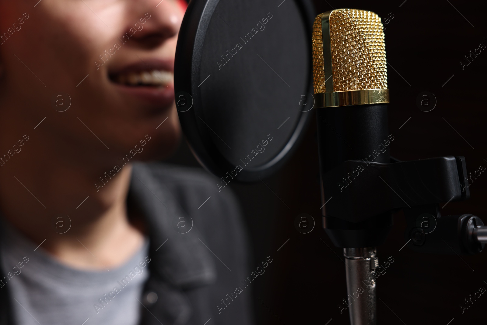 Photo of Vocalist singing into microphone in professional record studio, closeup