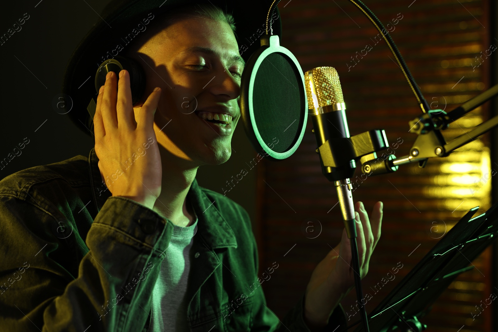 Photo of Vocalist with headphones singing into microphone in professional record studio