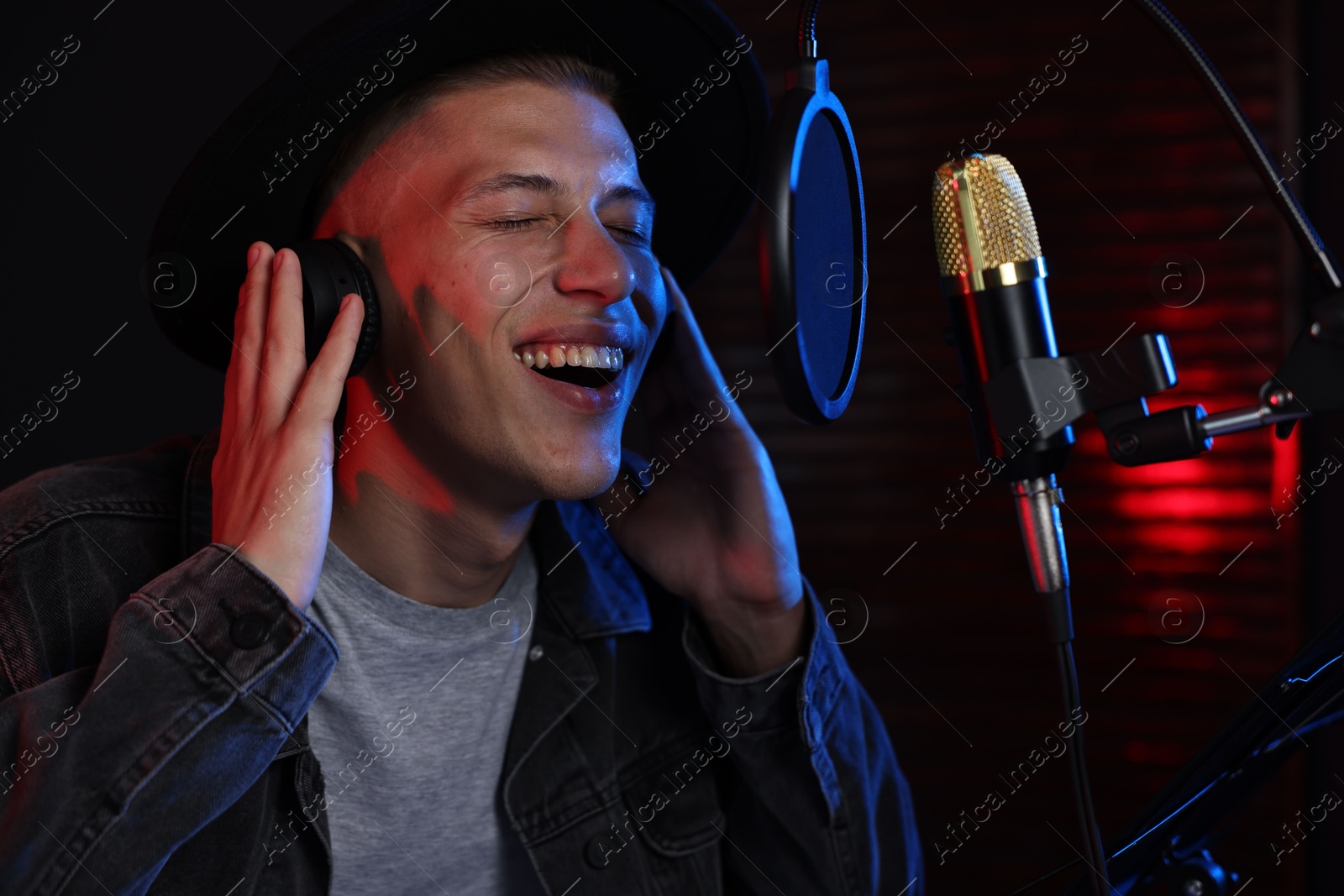 Photo of Vocalist with headphones singing into microphone in professional record studio