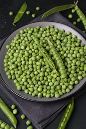 Fresh green peas and pods on black table