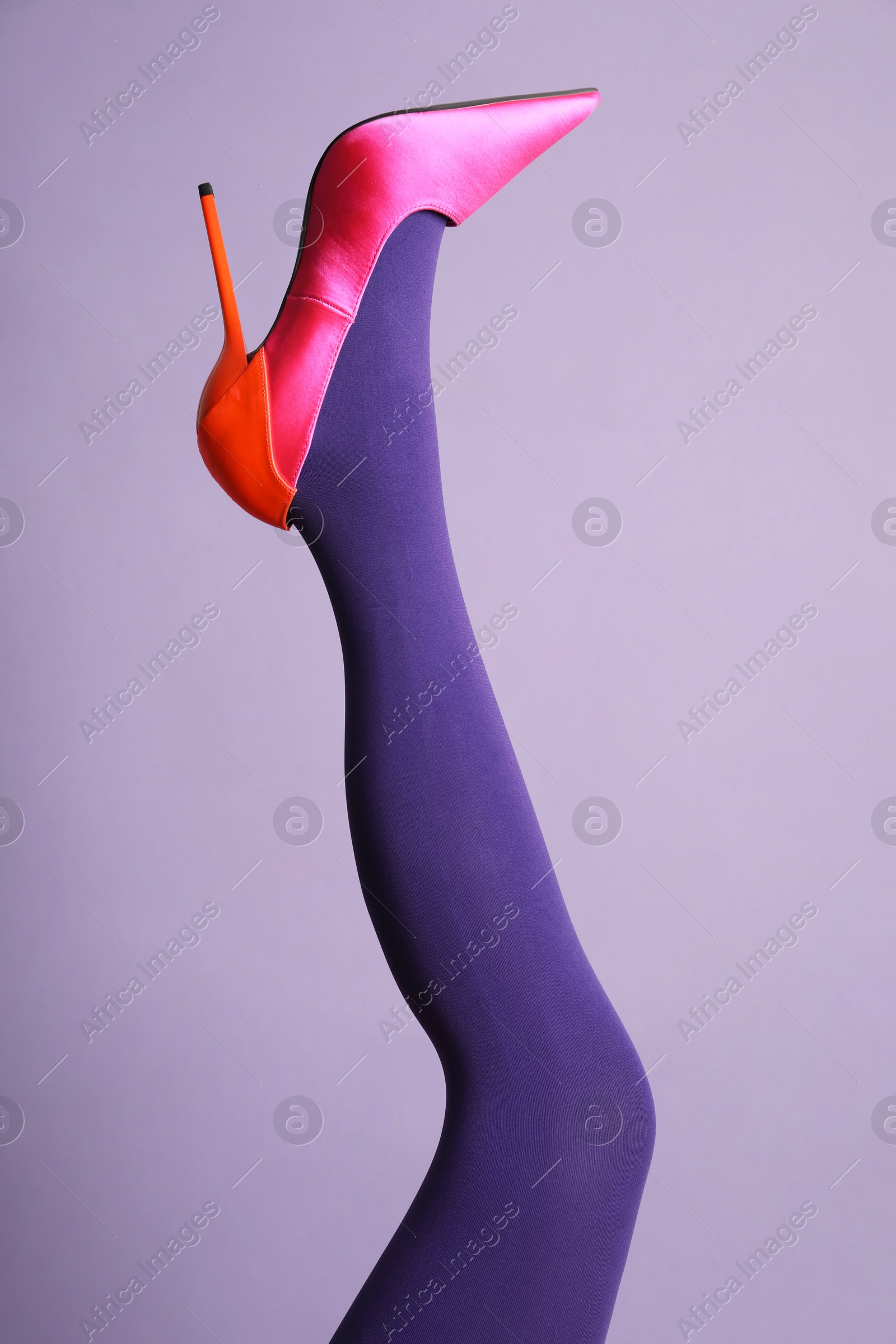 Photo of Woman wearing bright tights and high heel shoe on violet background, closeup