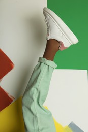 Woman wearing sneakers on color background, closeup