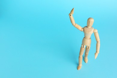 Wooden human model on light blue background, space for text. Mini mannequin