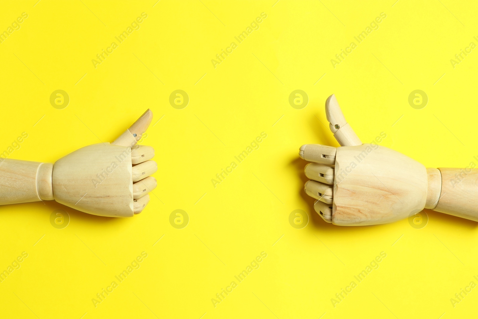 Photo of Wooden mannequin hands on yellow background, flat lay