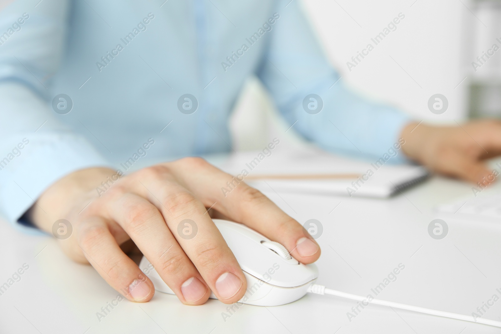 Photo of Man working with wired mouse at white table indoors, closeup