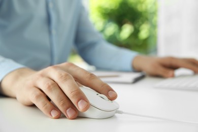 Photo of Man working with wired mouse at white table indoors, closeup