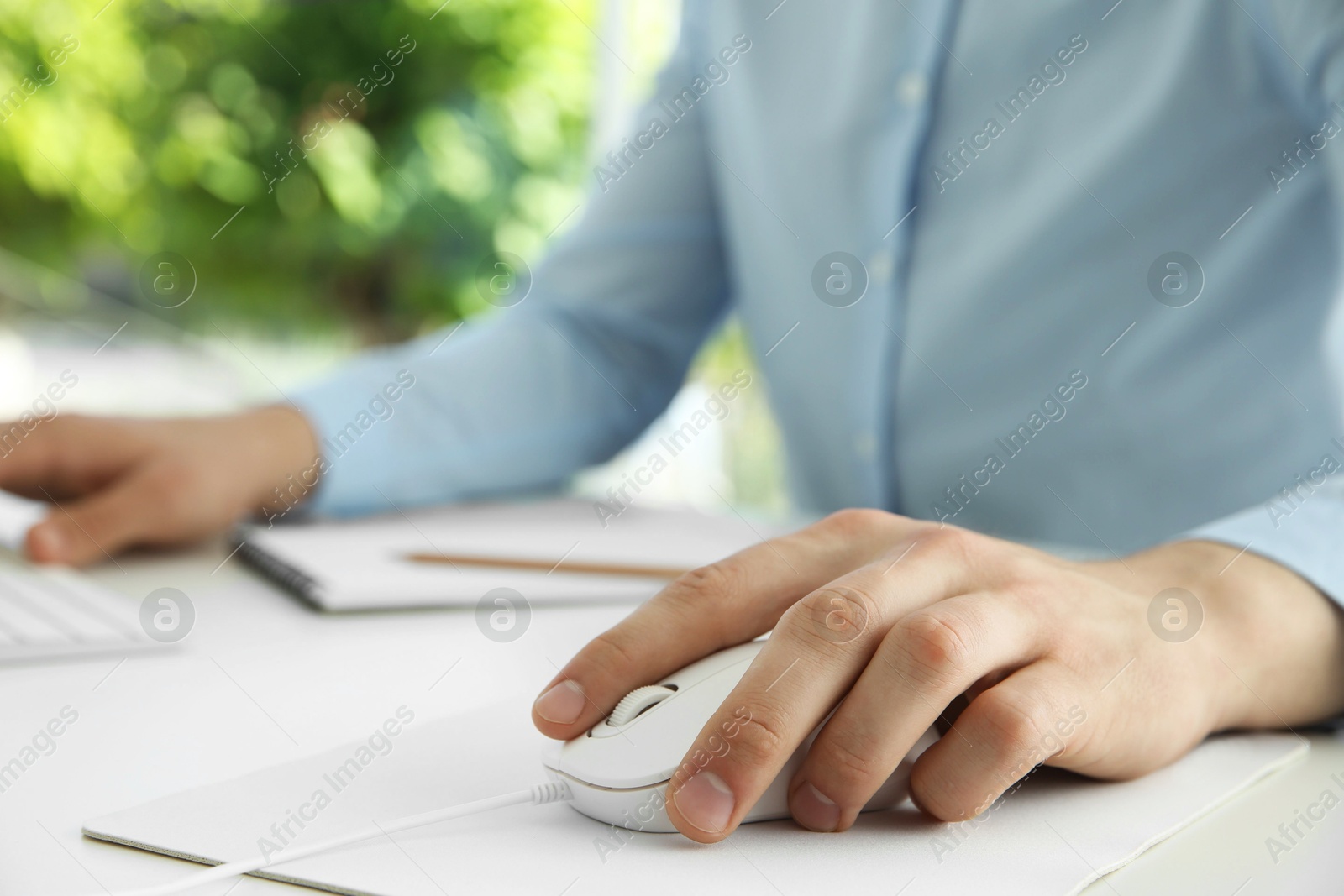 Photo of Man working with wired mouse at white table indoors, closeup