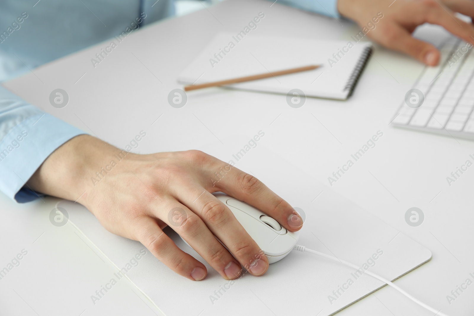 Photo of Man working with wired mouse and computer keyboard at white table indoors, closeup