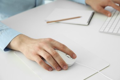 Man working with wired mouse and computer keyboard at white table indoors, closeup