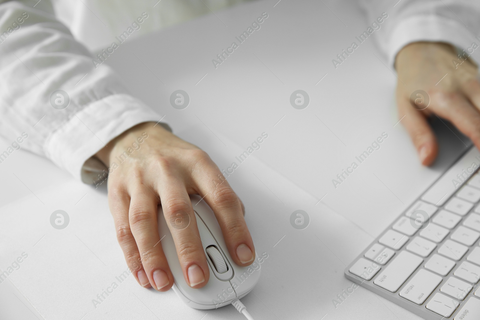 Photo of Woman working with wired mouse and computer keyboard at white table, closeup