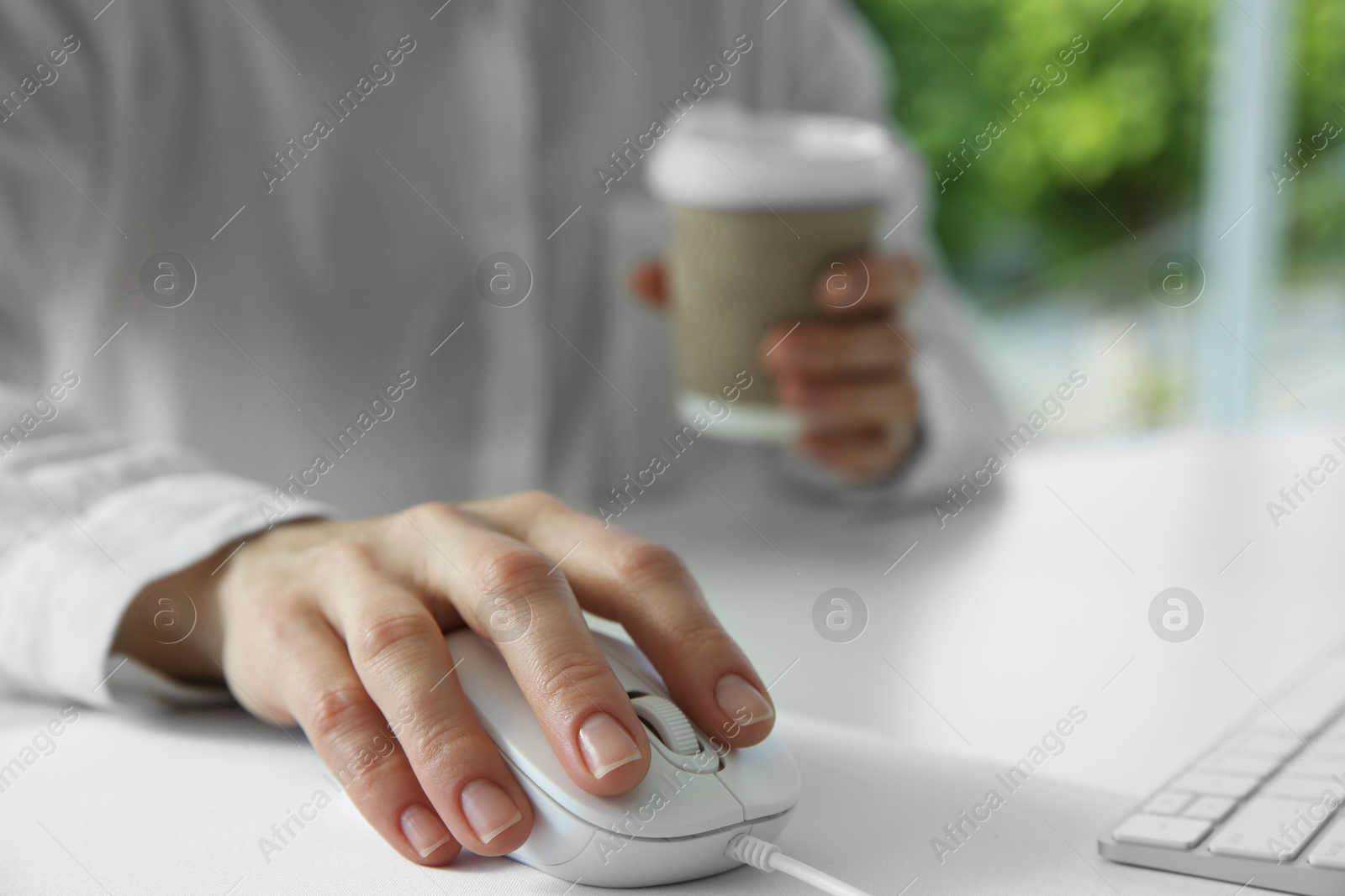 Photo of Woman with wired mouse and paper cup at white table indoors, closeup