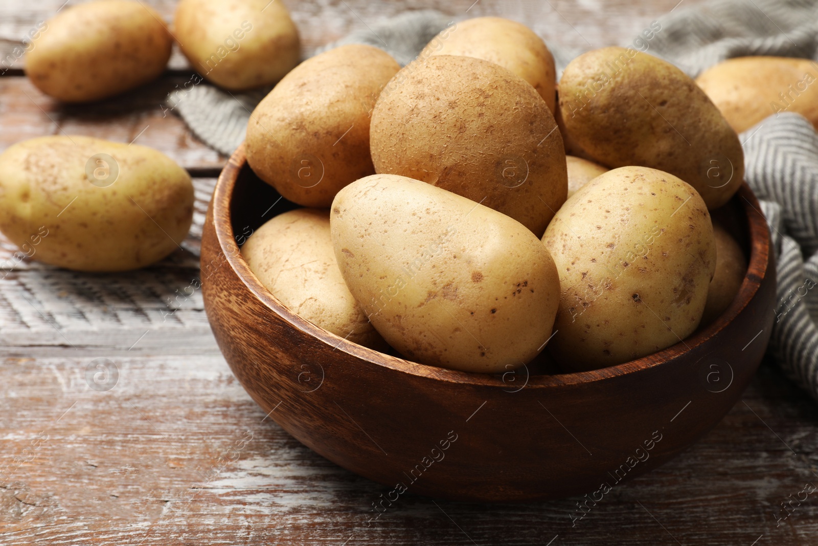 Photo of Many fresh potatoes in bowl on wooden rustic table, closeup