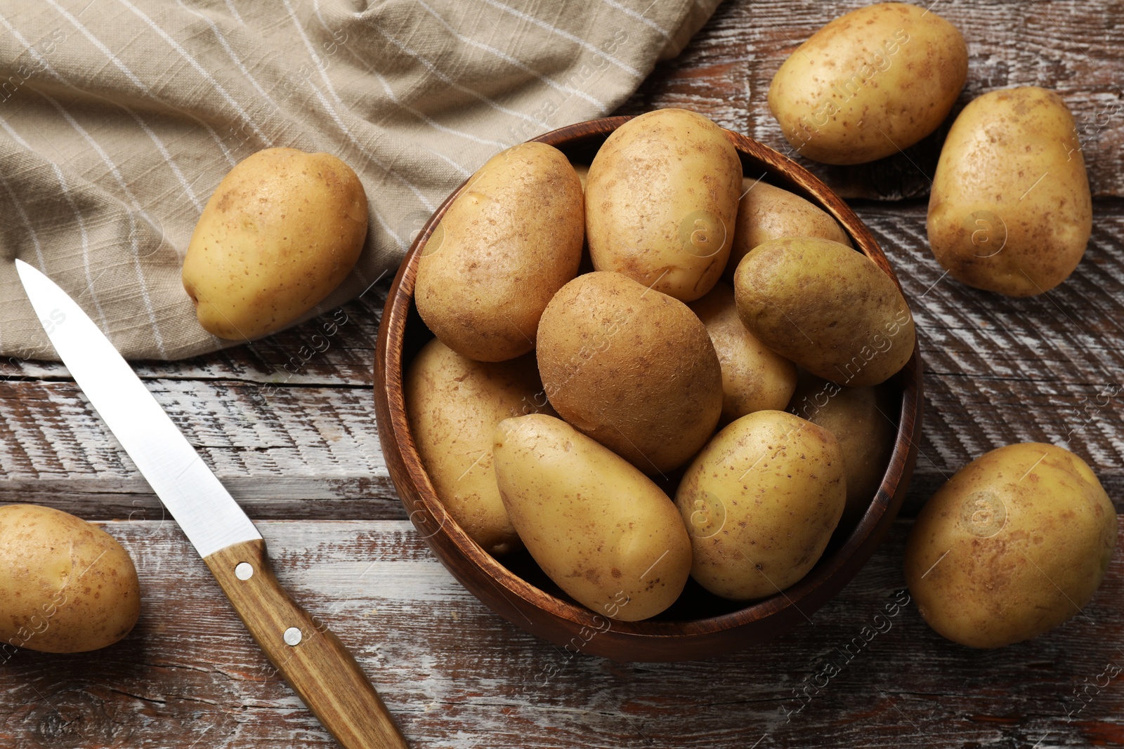 Photo of Many fresh potatoes, bowl and knife on wooden rustic table, flat lay