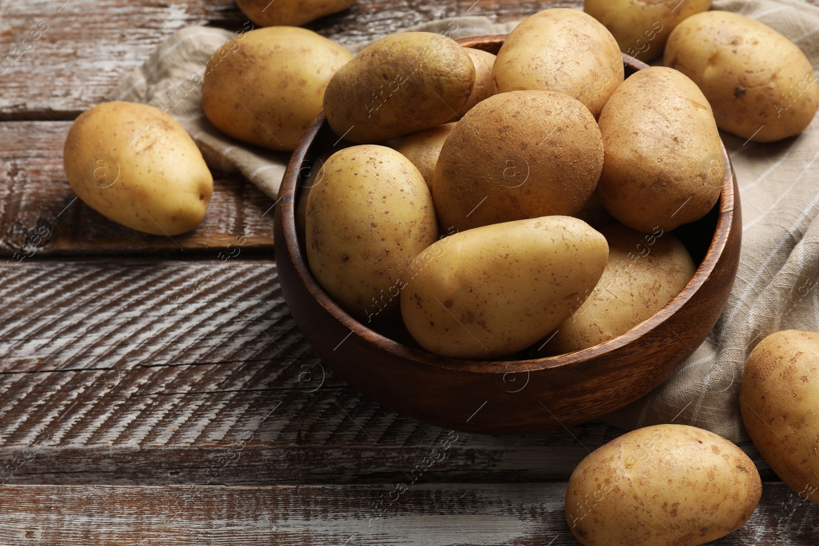 Photo of Many fresh potatoes in bowl on wooden rustic table, above view