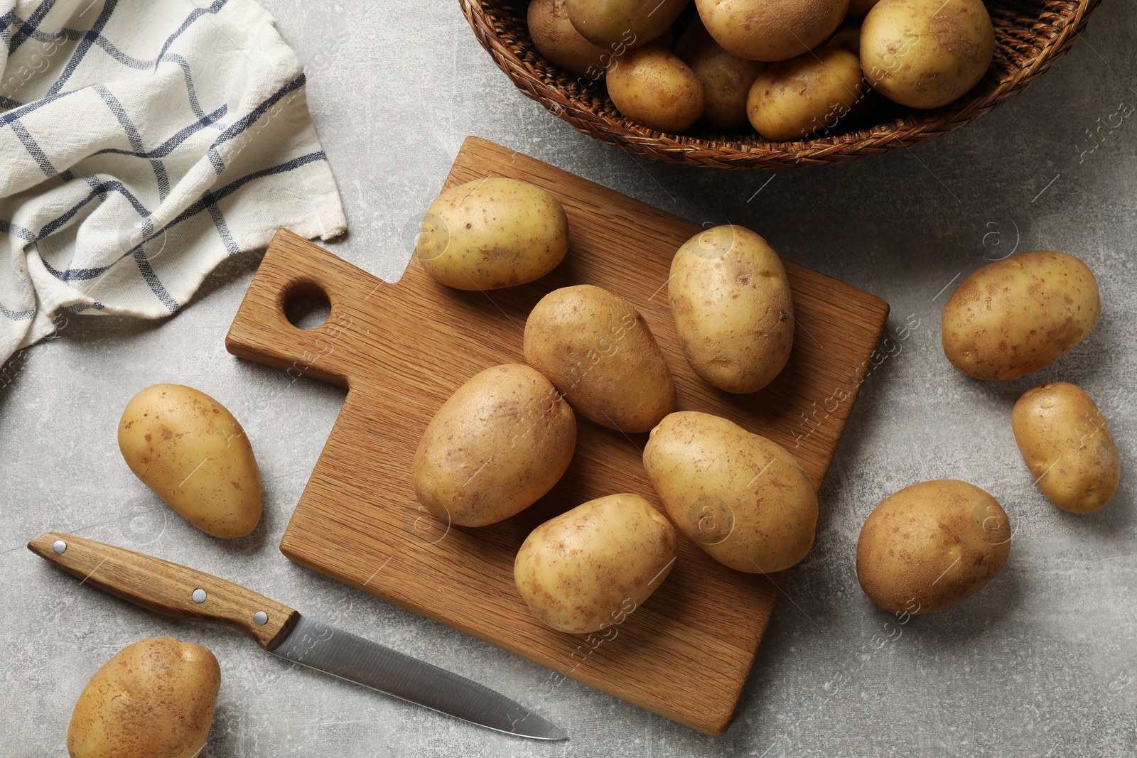 Photo of Many fresh potatoes, board and knife on grey table, flat lay