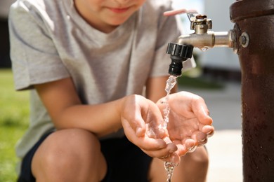 Photo of Water scarcity. Little boy drinking water from tap outdoors, closeup