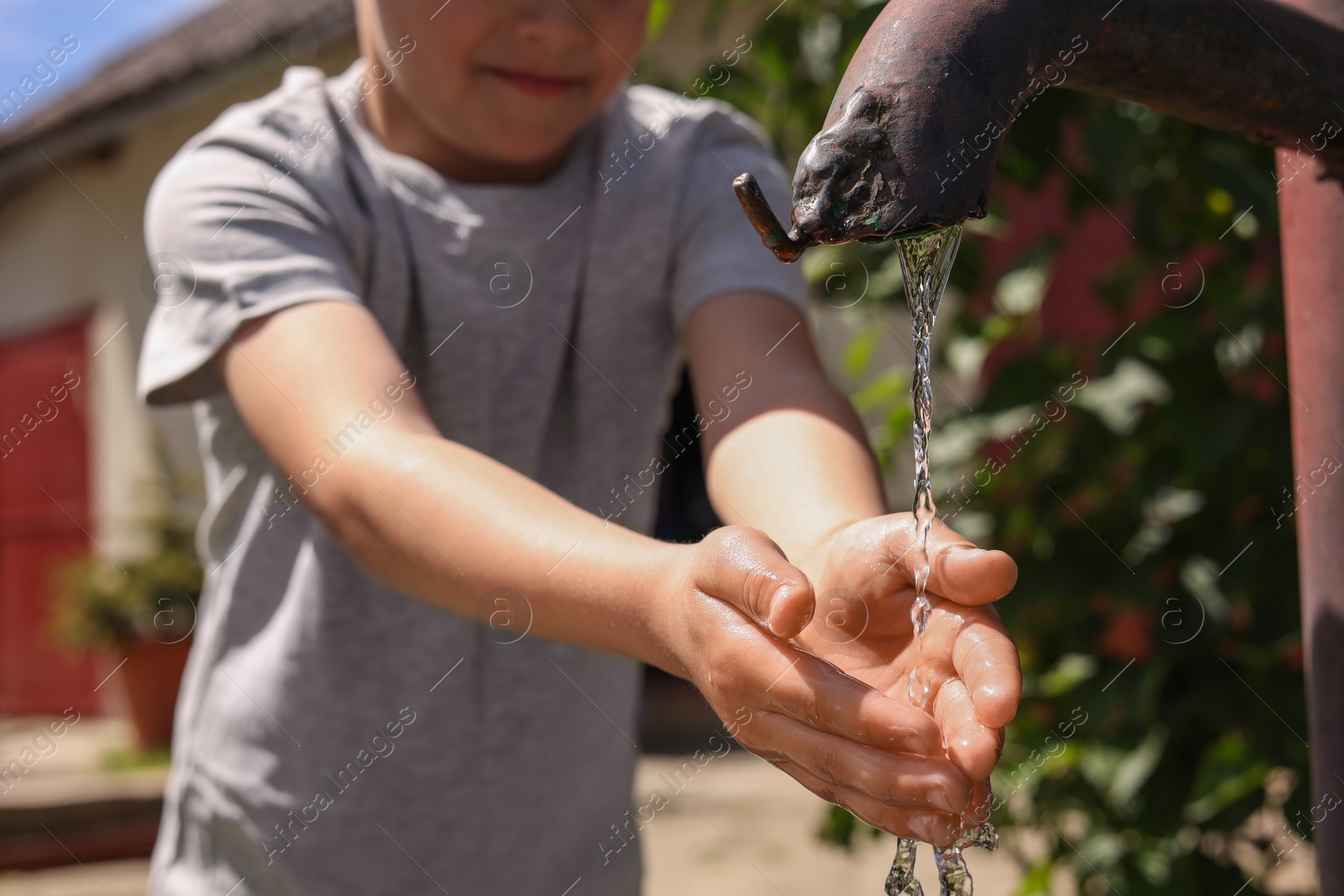 Photo of Water scarcity. Little boy drawing water with hands from tap outdoors, closeup