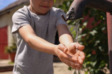 Photo of Water scarcity. Little boy drawing water with hands from tap outdoors, closeup