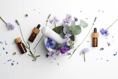 Photo of Aromatherapy. Essential oils, flowers, eucalyptus leaves, mortar and pestle on white background, flat lay