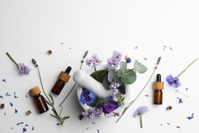 Photo of Aromatherapy. Essential oils, flowers, eucalyptus leaves, mortar and pestle on white background, flat lay