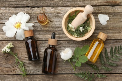 Aromatherapy. Different essential oils, flowers, green leaves, mortar and pestle on wooden table, flat lay