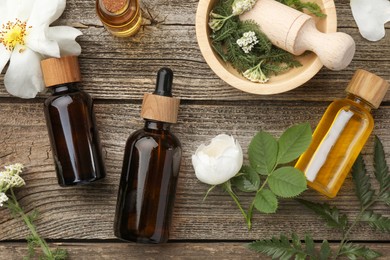 Photo of Aromatherapy. Different essential oils, flowers, green leaves, mortar and pestle on wooden table, flat lay