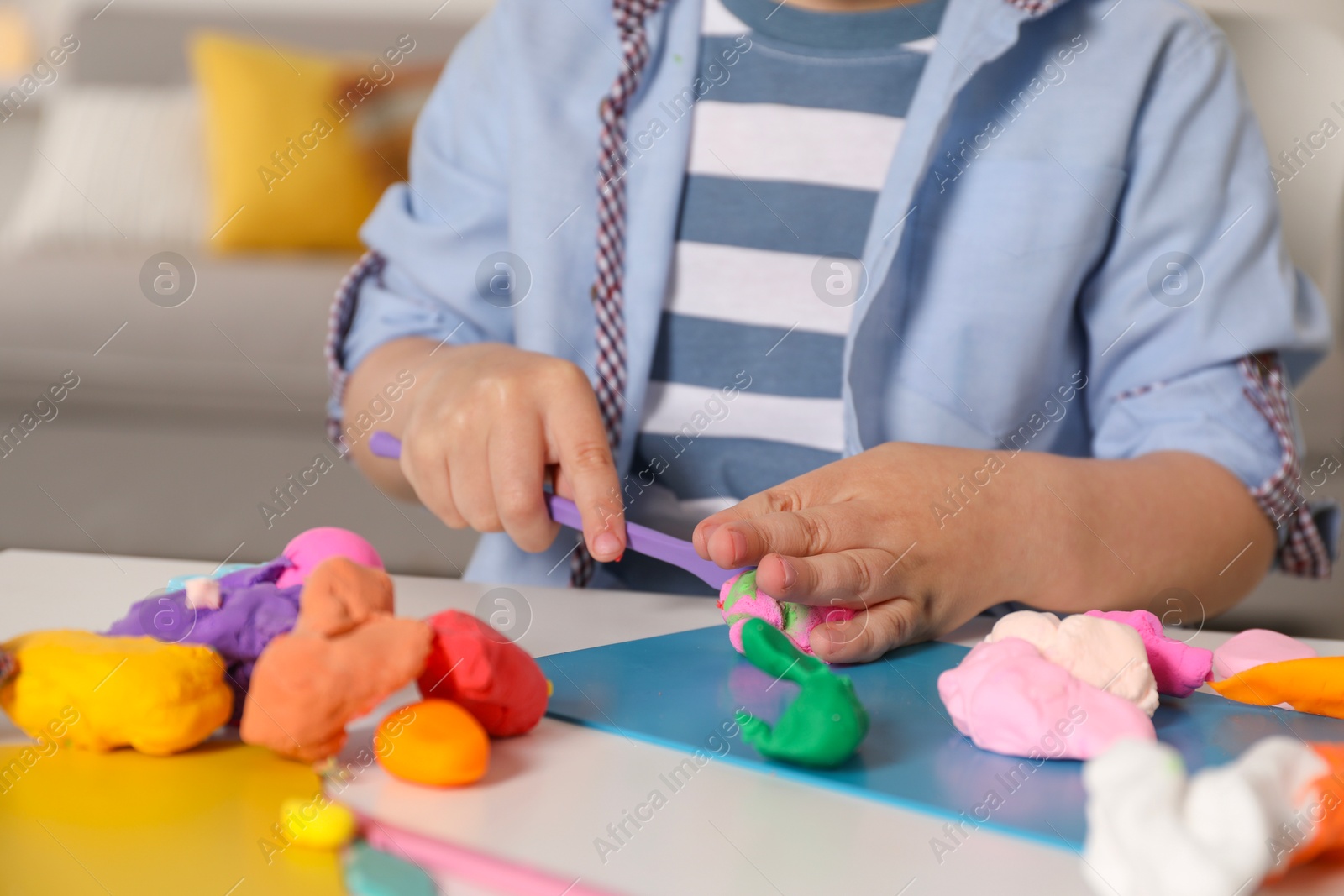 Photo of Little boy sculpting with play dough at table indoors, closeup