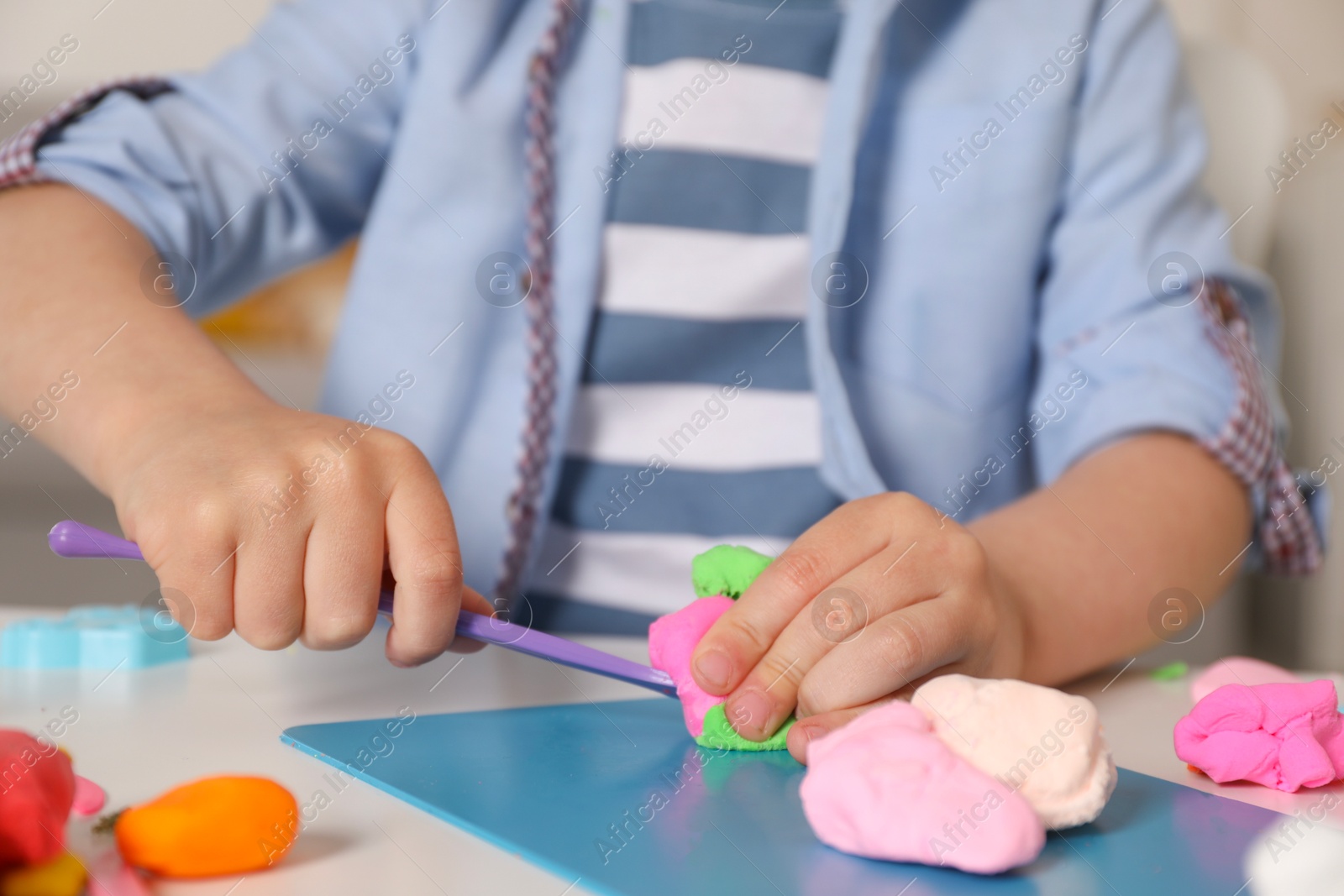 Photo of Little boy sculpting with play dough at table indoors, closeup