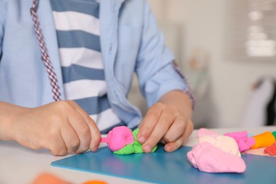 Photo of Little boy sculpting with play dough at table indoors, closeup