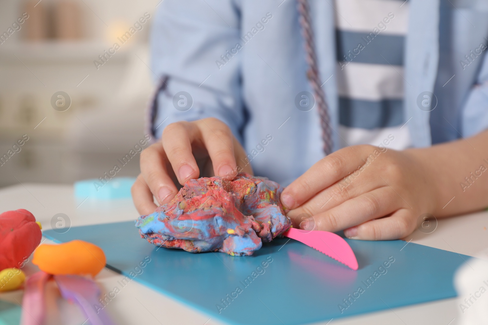 Photo of Little boy sculpting with play dough at table indoors, closeup