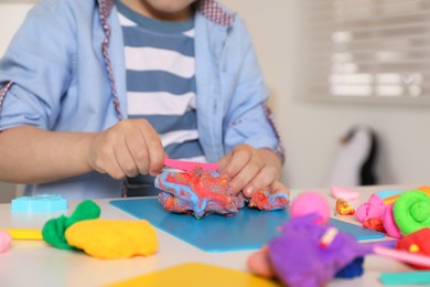 Photo of Little boy sculpting with play dough at table indoors, closeup