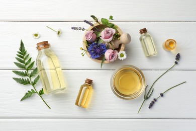 Aromatherapy. Different essential oils, green twig and flowers on white wooden table, flat lay